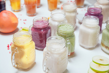 Glass jars with fresh delicious smoothie and straw on white table.