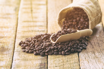 Coffee beans in gunny sack. Close up or  macro concept of roasted black coffee beans for background,texture and wallpaper. Pour coffee beans from gunny sack on rustic wood table.