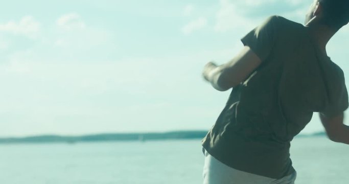Young adult African American man enjoying summer day, throwing rocks into water. 4K UHD RAW edited footage