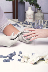 Obraz na płótnie Canvas Closeup finger nail care by manicure specialist in beauty salon. Manicurist clear cuticle professional scissors for manicure and pedicure.
