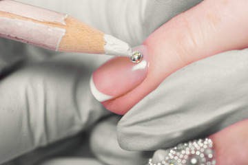 Closeup finger nail care by manicure specialist in beauty salon. Manicurist Glues rhinestones on...