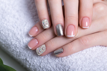 Beautiful classic French manicure with rhinestones on female hand. Close-up. Picture taken in the studio on the background of flowers