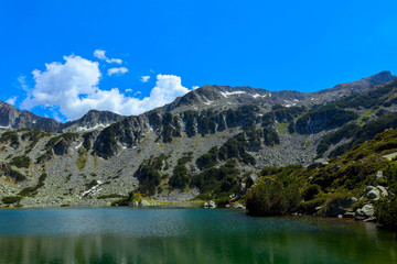 Fototapeta na wymiar Beautiful mountains lake with a reflection of the high green mountains peaks, on the blue sky background. Amazing Mountain hiking paradise landscape with a lake, no people.