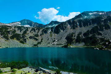 Beautiful mountains lake with a reflection of the high green mountains peaks, on the blue sky background. Amazing Mountain hiking paradise landscape with a lake, no people.