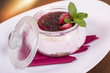 Delicious pudding with chocolate flakes and strawberries in a glass jar on the wooden table. Tiramisu in a glass cup. Close up of a delicious dessert.