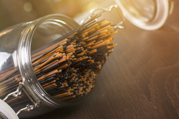 Close up of a jar with raw spaghetti and macaroni. Many different spaghetti, dough and cooking utensils on the wooden table.