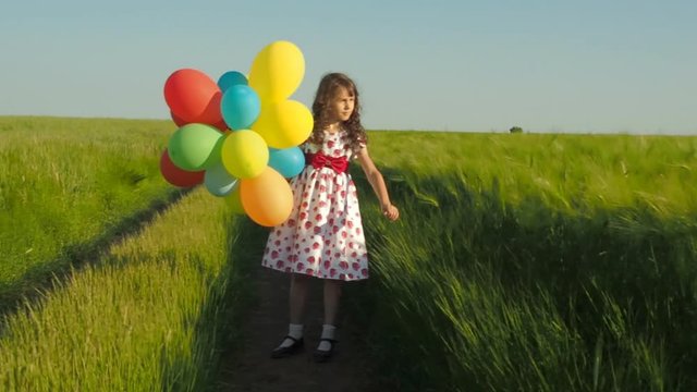 Little girl with balloons in the field. The girl is stroking the wheat field.