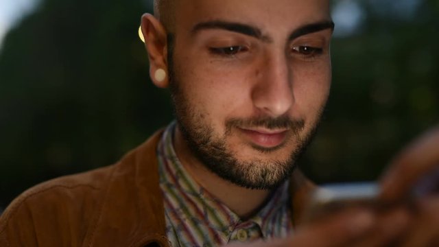 Portrait of young man gay using smart phone, face illuminated by screen light &ndash; night life, intenret, communication concept