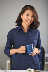 Portrait of young Asian woman in dark-blue shirt posing with coffee mug