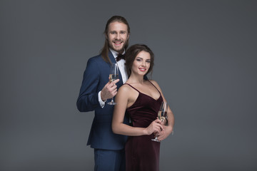 smiling couple in evening fashion outfit holding glasses with champagne