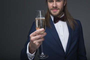 smiling man in tuxedo holding glass with champagne and looking at camera