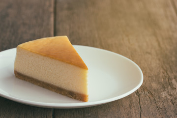 Homemade New York style cheesecake on white plate. Moist and smooth baked cheesecake. Delicious plain New York cheesecake with golden brown surface on rustic wood table with copy space for background.