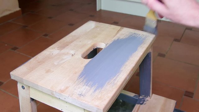 Man's hand paints the furniture step stool . Gray coating. Painting step stool with grey color