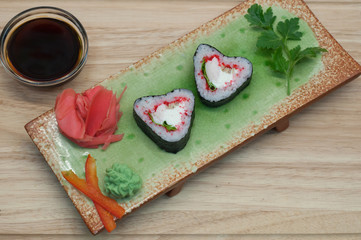 Роллы в форме сердца с имбирем и васаби на зеленой тарелке