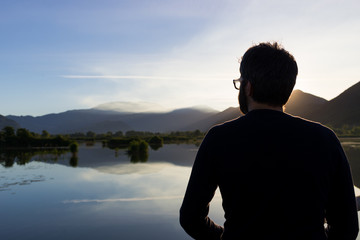 Fototapeta premium Man looking at beautiful sunrise sunset reflection at Iseo lake in Italy in summer
