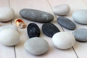 Sea grey and white round pebbles on wooden table with a piece of shell