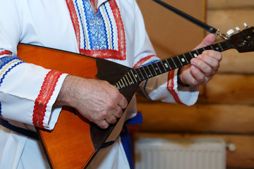 Balalaika wooden in the hands of the musician. Slavic Russian national costume with embroidery....