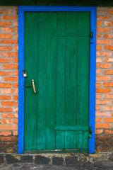 Old barn with wooden doors of green color and brick wall