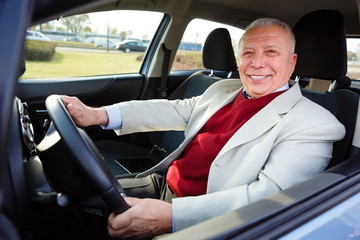happy elderly man with white smile driving a car - looking in camera