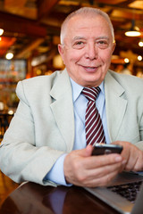 Well-dressed old senior businessman on smartphone connected to wireless internet sharing photo in social networks