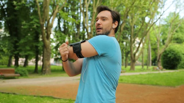 Handsome fitness man doing stretching exercises with hands and neck in the park before run. Showing thumps up. Slow motion. Close up