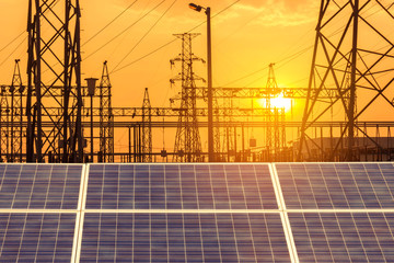  solar cells in power station with  high voltage electric pillars substation on sunset.   