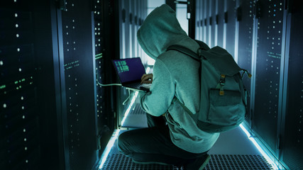A Hooded Hacker With Laptop Connects to Rack Server and Steals Information from Corporate Data...