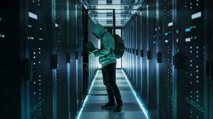 A Hooded Hacker With Laptop Connects to Rack Server and Steals Information from Corporate Data Center.