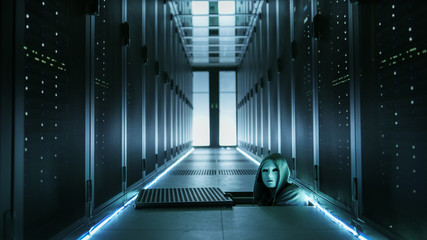 Hooded Hacker in a Mask Watching From Under Floor Hatch in Data Center with Rows of Rack Servers.