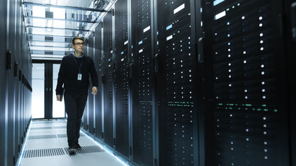 IT Engineer Holding Notebook and Walking Through Data Center Full of Working Rack Servers.