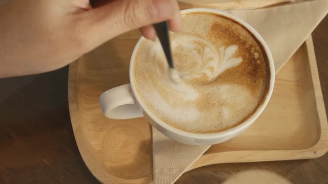 Panning shot of A woman holding coffee spoon to stir hot coffee on wooden table