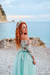 Young beautiful red-haired woman in a luxurious dress standing on a rocky shore of the Adriatic Sea, close-up