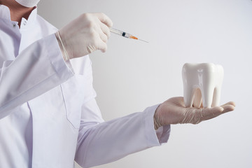 Dentist doing injection into the tooth in dental clinic. Dentist holding a syringe with anesthesia and white healthy prosthetic tooth in the dentist's office on isolate white background.