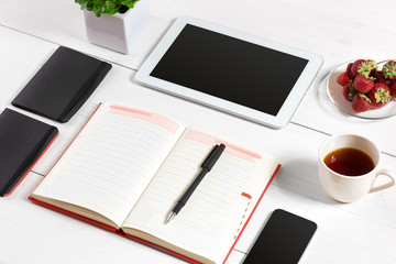 Office table desk with set of supplies, white blank notepad, cup, pen, tablet, glasses, flower on white background. Top view