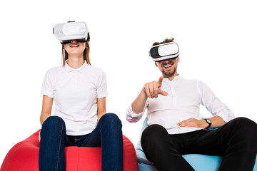 Excited young couple experiencing virtual reality seated on beanbags isolated on white background