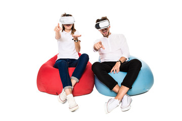 Excited young couple experiencing virtual reality seated on beanbags isolated on white background