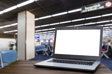 Laptop computer with white blank screen on wooden table with blurred in airport terminal waiting room, selective focus, copy space, working outside office, online social media, searching data concept