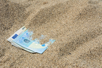 Fototapeta na wymiar Geld im Urlaub - Banknoten im Sand vergraben