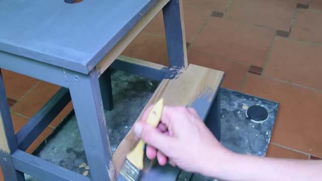 Man's hand paints the furniture step stool . Gray coating. Painting step stool with grey color