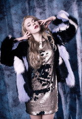 Attractive young woman posing in sequin dress and blue fur coat. Studio image