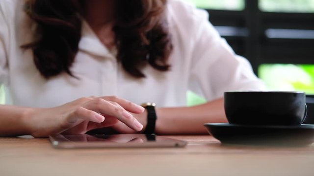 A woman touching and sliding on tablet pc on wooden table in cafe
