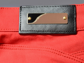 Gold metal and black leather empty label on red denim