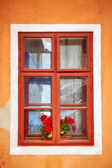 Closed old window with red flowers in orange wall.