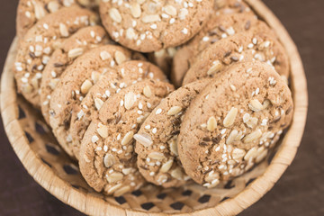 A delicious homemade cookie with cereals and seeds lies in a wicker basket on a saturated brown background