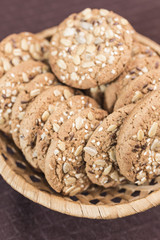 Homemade fitness cookies with cereals and sunflower seeds lies in a wicker basket on a dark brown background, a vertical frame