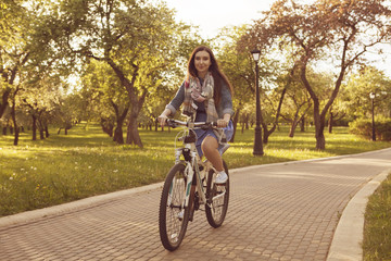 Beautiful smiling girl on bicycle in the blossom park. Soft summer light
