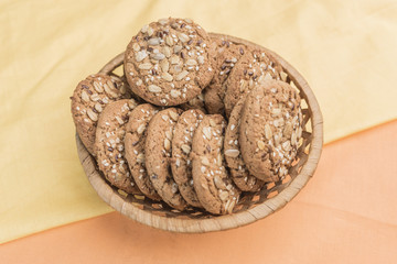 Homemade cookies with cereals in a wicker basket on a gentle pear-yellow and warm light orange background
