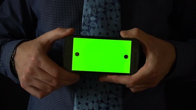 Man holds smartphone to camera with green screen.