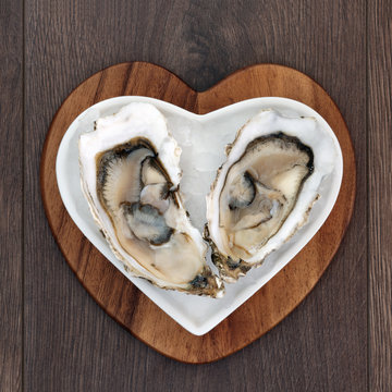 Oysters on crushed ice in a heart shaped plate on a maple wood board over old oak background.
