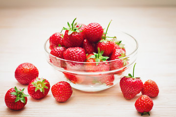 Fresh strawberries in bowl on white wooden background.